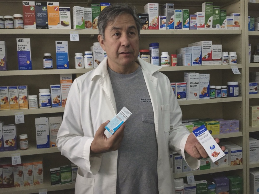 A pharmacist reading supplement labels in a pharmacy aisle